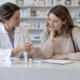 Une pharmacienne présente un tube homéopathique à une patiente au comptoir.