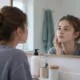 Une adolescente observe dans un miroir quelques boutons sur sa joue.