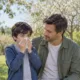 Un enfant utilise un mouchoir à côté de son père dans un jardin.