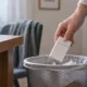Une main dépose un paquet de cigarettes fermé dans une corbeille.