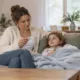 Un parent lit un thermomètre à côté de son enfant allongé sur le canapé.