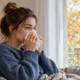 Une jeune femme utilise un mouchoir près d’une fenêtre.