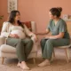 Une femme enceinte assise échange avec une sage-femme dans une salle de maternité.
