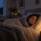 Femme éveillée dans son lit, la tête sur l’oreiller, dans une chambre faiblement éclairée.