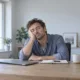 Un homme somnole devant son ordinateur dans un bureau éclairé par la lumière du jour.